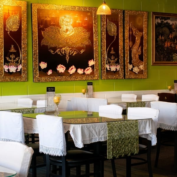 Restaurant interior with lime green walls, Thai art, glass tables, and white chair covers.
