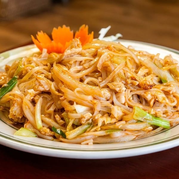 A plate of Pad See Ew with wide noodles, chicken, and green onions, garnished with a carrot flower.