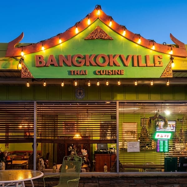 Exterior of Bangkokville Thai Cuisine at dusk, with illuminated sign and outdoor seating.